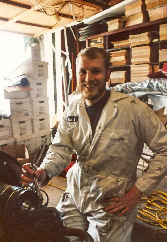 Technician checks a car battery with a multimeter in a hot garage