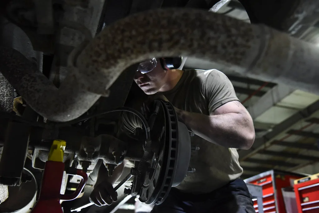 Gloved hands measuring car brake pad thickness beside an exposed rotor