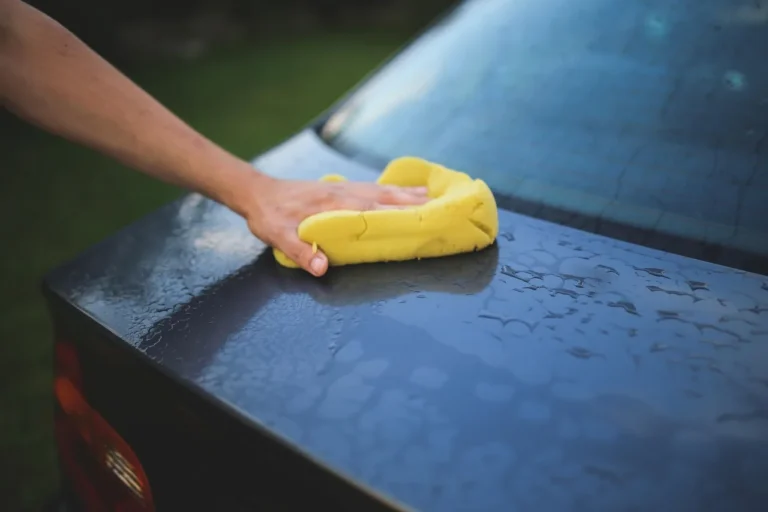 Car cleaning and restoration scene with buckets, microfiber towels, and a person cleaning a sedan in natural light.