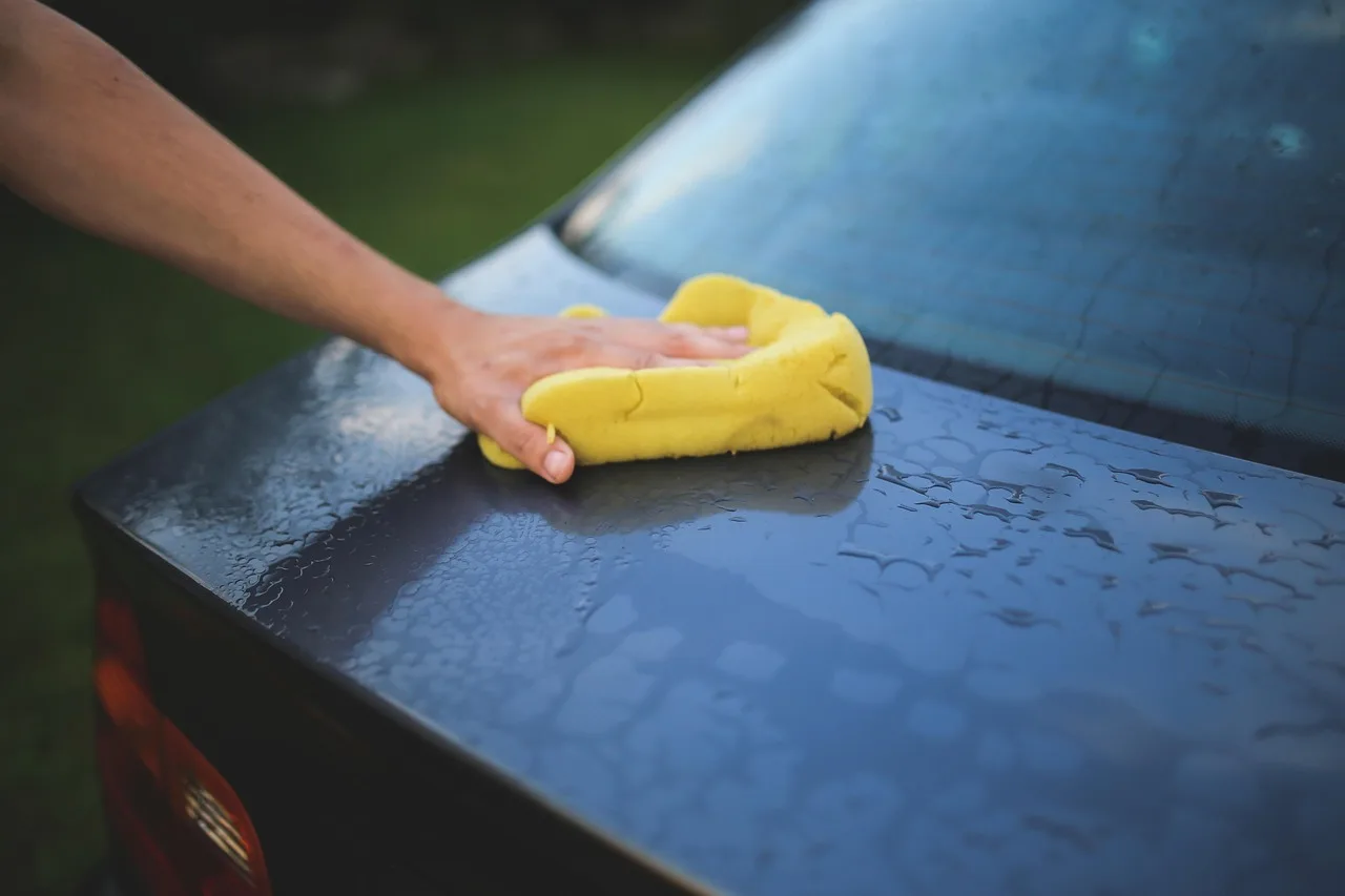 Car cleaning and restoration scene with buckets, microfiber towels, and a person cleaning a sedan in natural light.