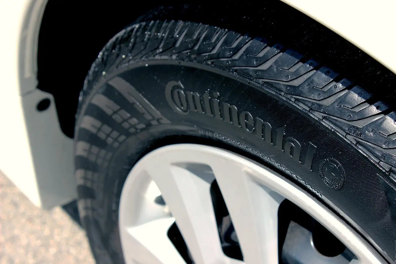 Driver checks car tire tread beside a sedan in bright driveway light.