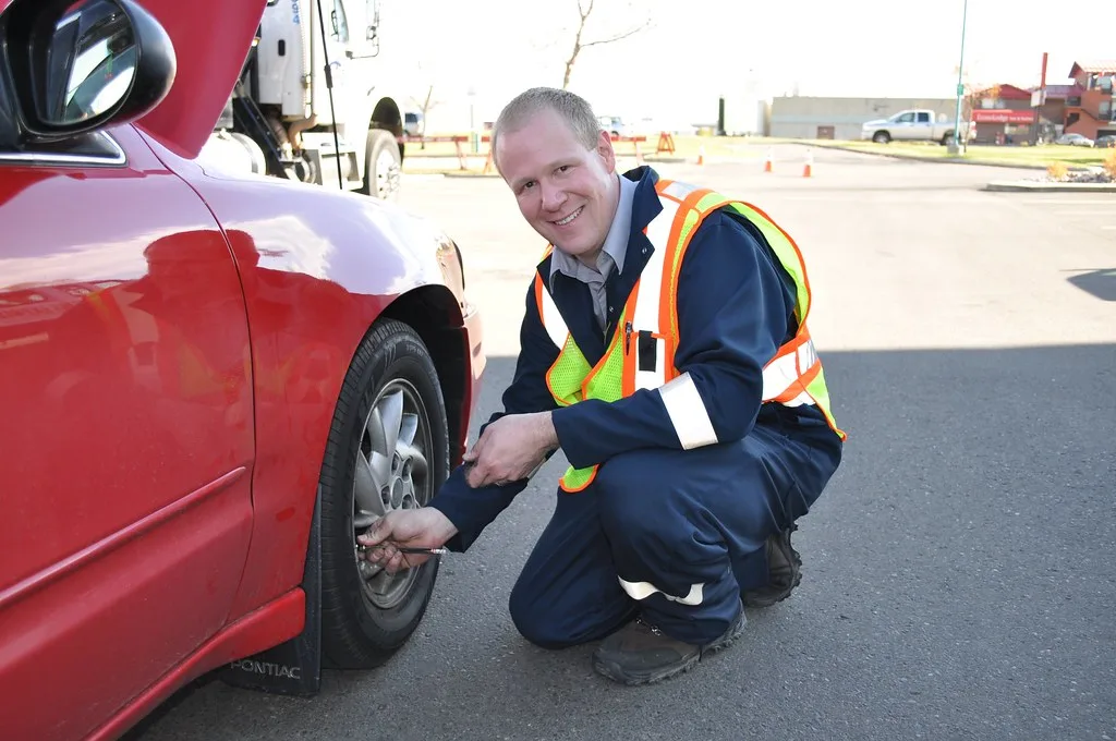 Hand uses a tire pressure gauge on a car tire valve stem in close-up.