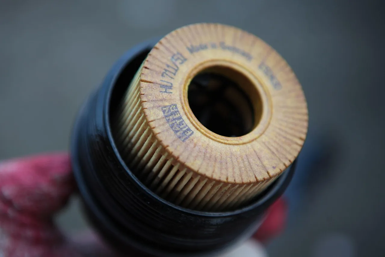 Mechanic and car owner inspecting an open engine bay with an oil dipstick and drain pan