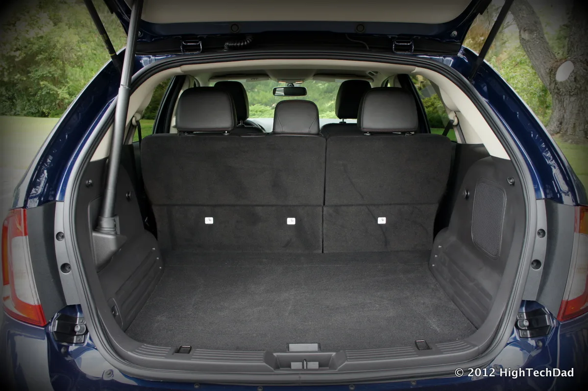 Folded stroller being loaded into a hatchback cargo area with a sedan nearby