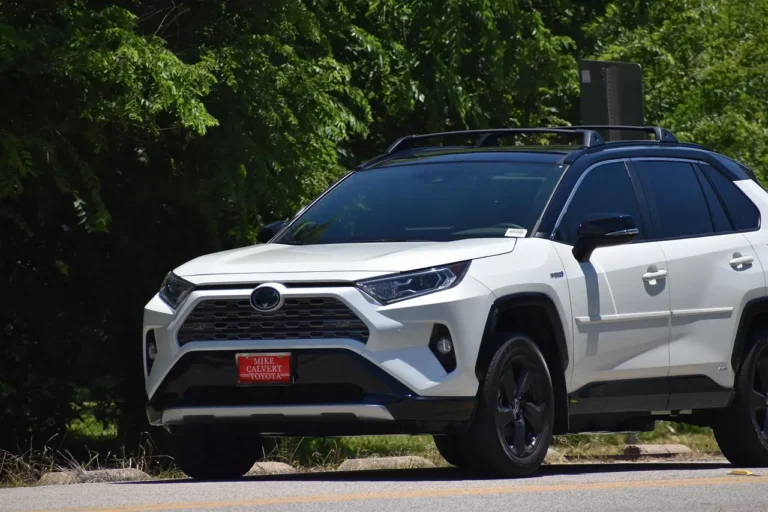 A crossover and SUV parked in a driveway with a parent loading groceries and a child entering one vehicle