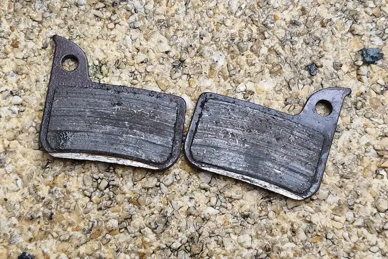 Hands comparing a worn brake pad and premium replacement pad on a workbench.