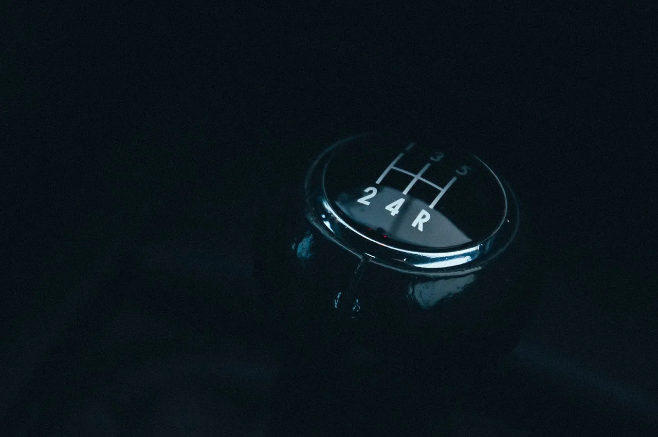 Driver using a manual gear shifter and clutch in a car interior with an automatic selector visible nearby
