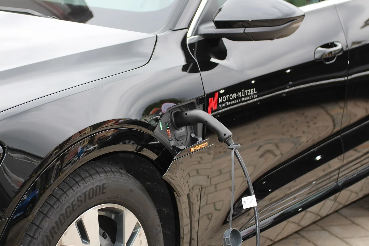 Older vehicle with hood open while hands inspect the car battery and cables in a garage