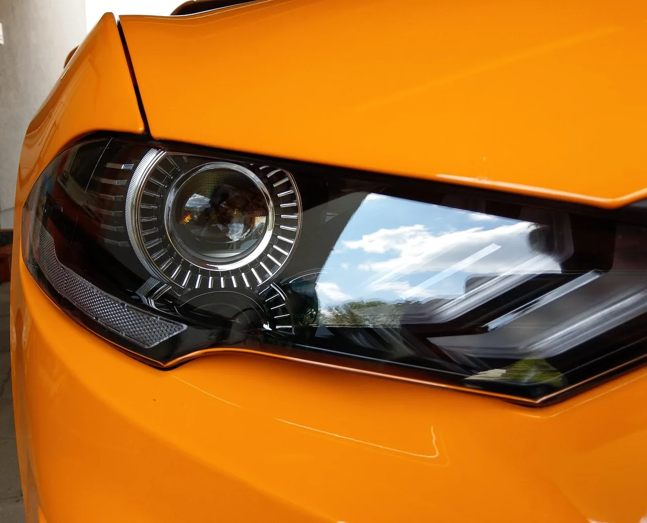 Older-car owner and mechanic compare headlight upgrade parts beside an open headlamp in a garage.