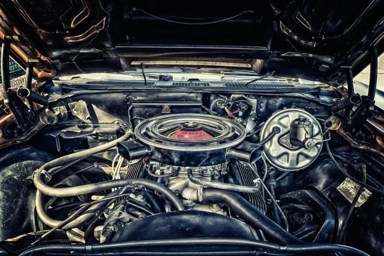Mechanic inspecting a high-mileage car engine with the hood open in a repair bay