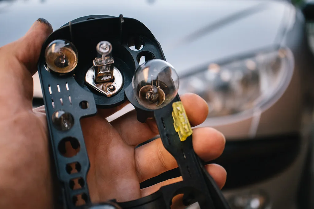 Gloved hands comparing OEM replacement bulbs next to a headlamp socket on a workbench