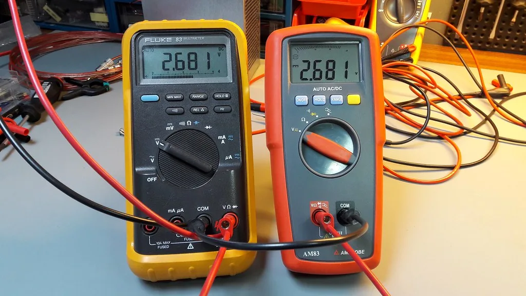 Beginner checking a car battery and fuse box under the hood with a multimeter