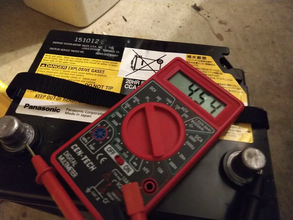 Hands using a multimeter on a car battery terminal during troubleshooting