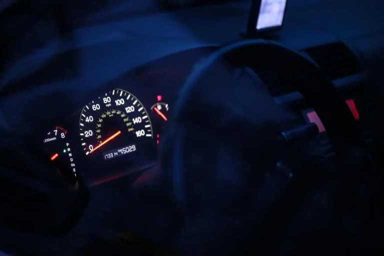 Beginner driver reaching for the car light switch on a dashboard at dusk