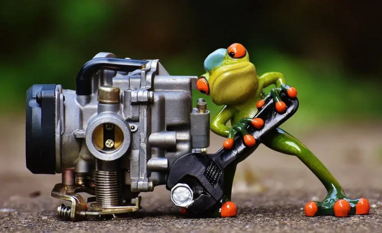 Mechanic comparing a disassembled carburetor and a fuel injector rail on a garage workbench.