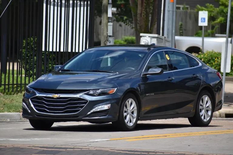 Chevy Malibu parked curbside while three adults review trim options on a clipboard in daylight