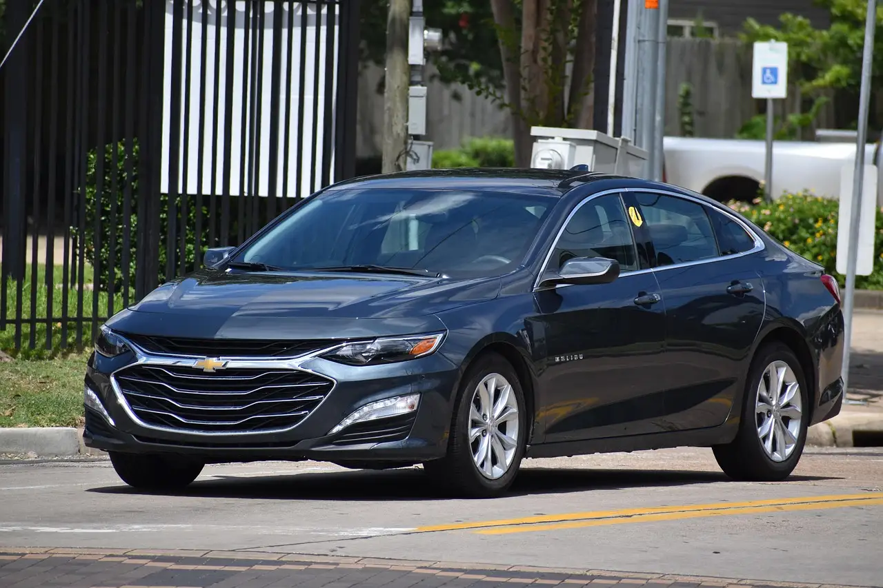 Chevy Malibu parked curbside while three adults review trim options on a clipboard in daylight