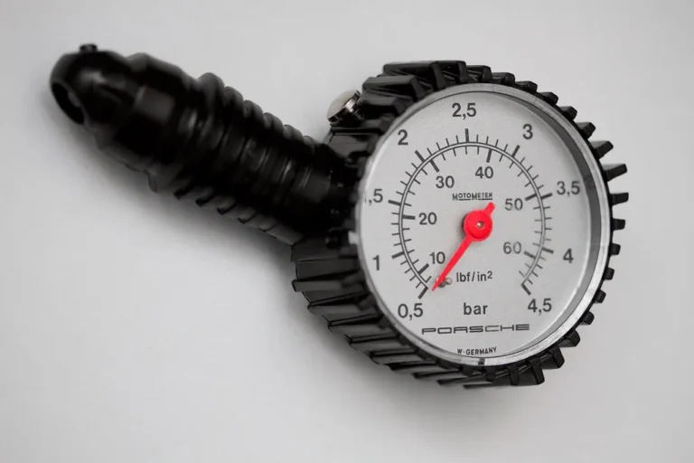 A person checks a car tire with digital and analog tire pressure gauges on a driveway.