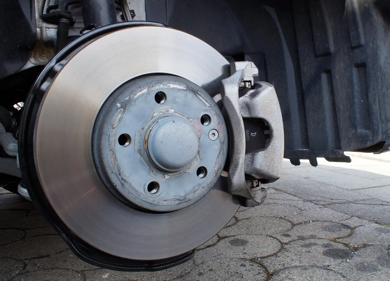 Mechanic inspecting a Ford sedan's front brake through the wheel spokes in daylight
