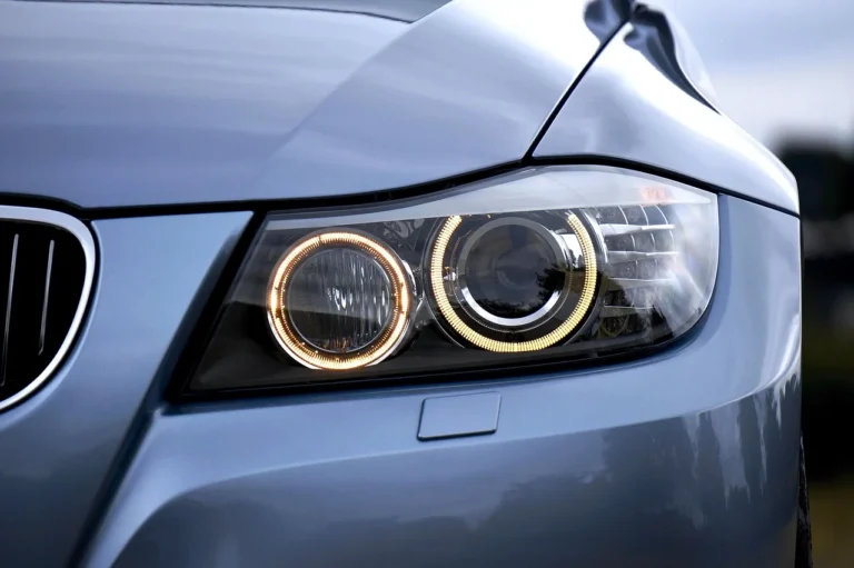Mechanic comparing halogen and LED car headlights beside a sedan in a workshop