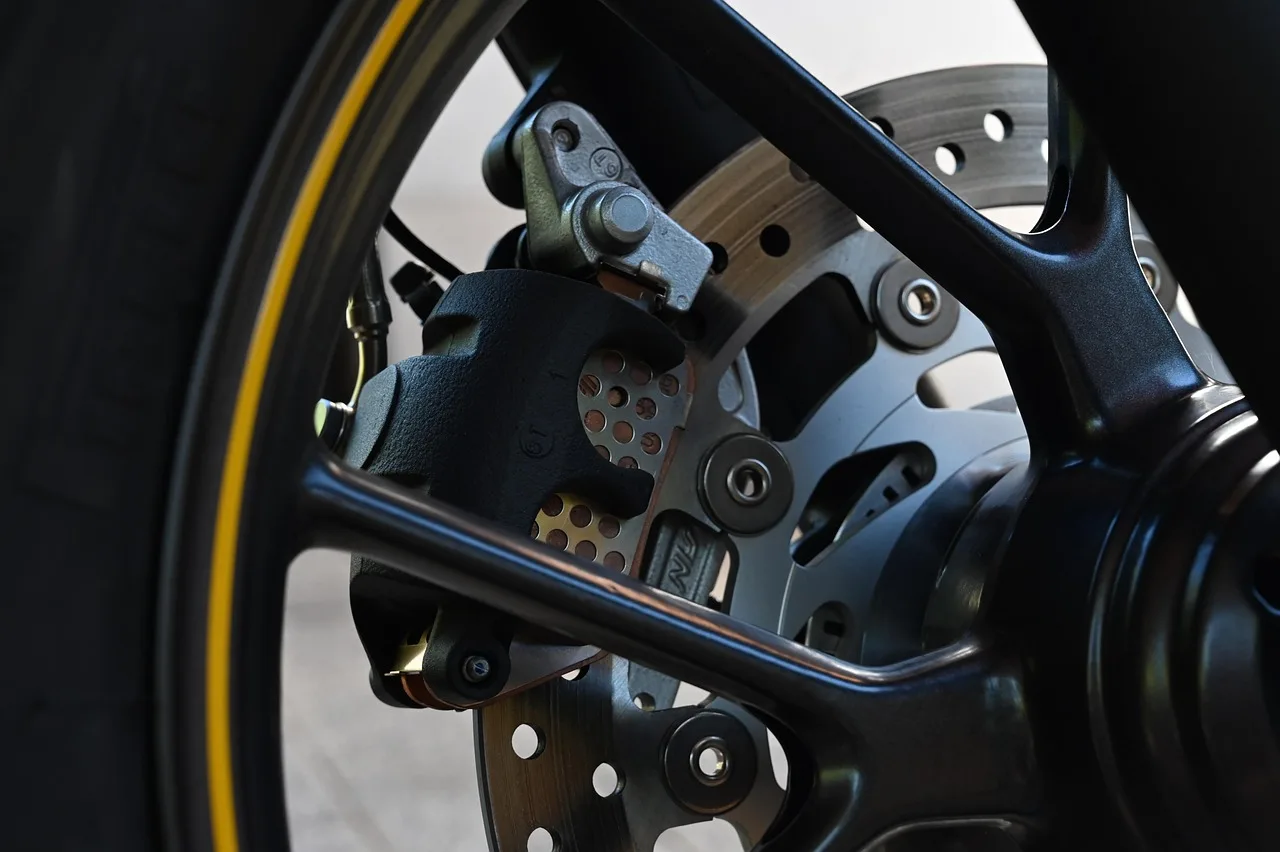 Mechanic inspecting a brake hose near a removed front wheel in a garage.