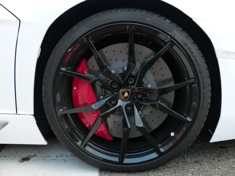 Homeowner checking car brakes with wheel off, showing rotor, caliper, and brake pad in daylight