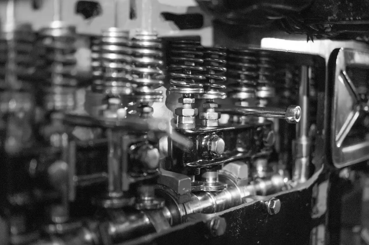 Mechanic beside an opened car engine cylinder head showing the valve area in natural garage light