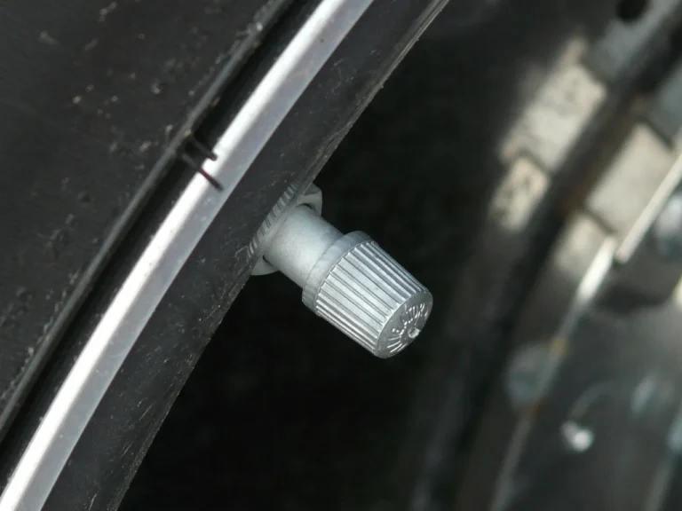 Driver checks a car tire with a pressure gauge beside the valve stem in morning light