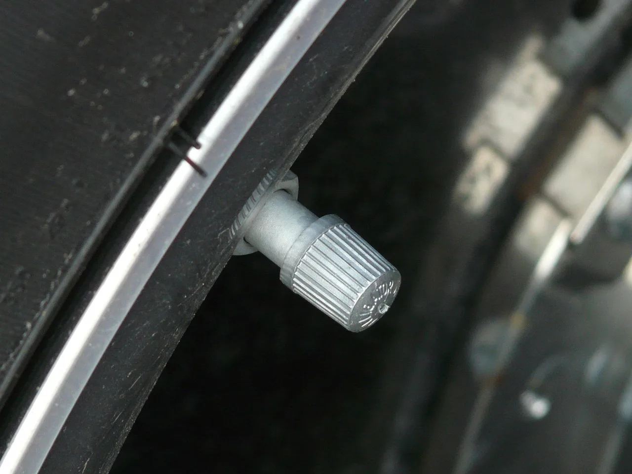 Driver checks a car tire with a pressure gauge beside the valve stem in morning light