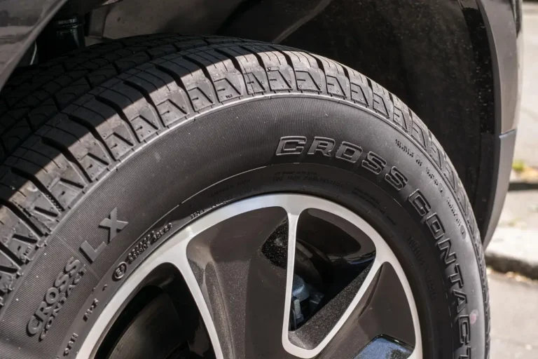Mechanic inspecting a sedan's front tires for uneven wear in a repair bay