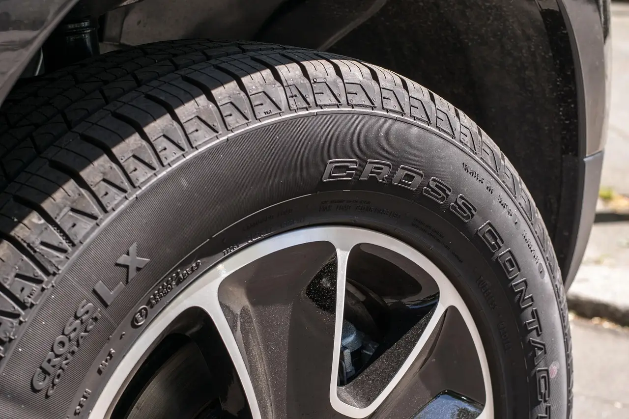 Mechanic inspecting a sedan's front tires for uneven wear in a repair bay